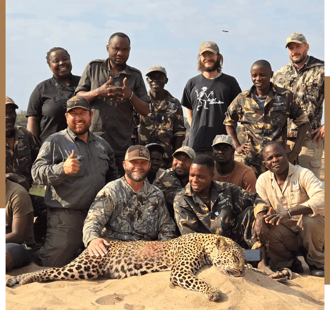 Group posing with a leopard in sand.